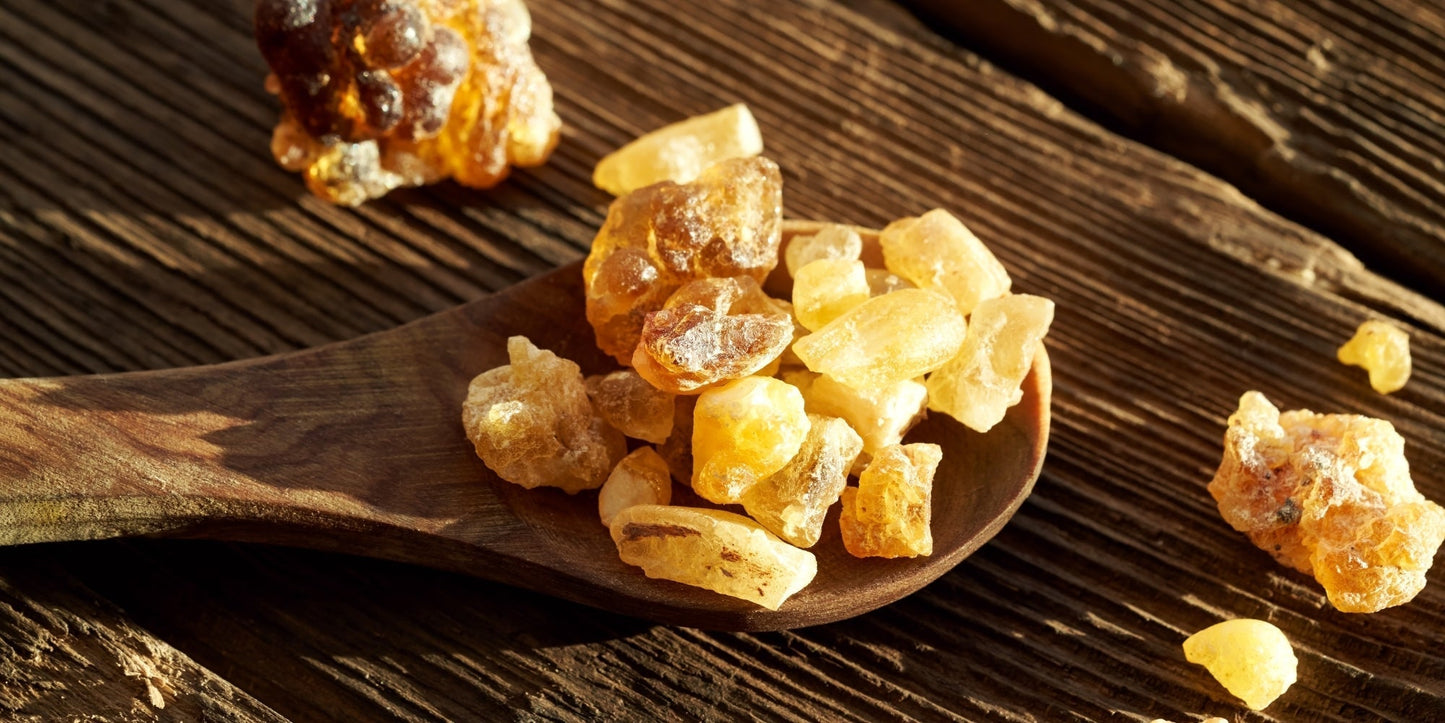 Three piles of frankincense resin tears in varying colors, representing Boswellia sacra, Boswellia carterii, and Boswellia frereana, displayed on a dark wooden surface.