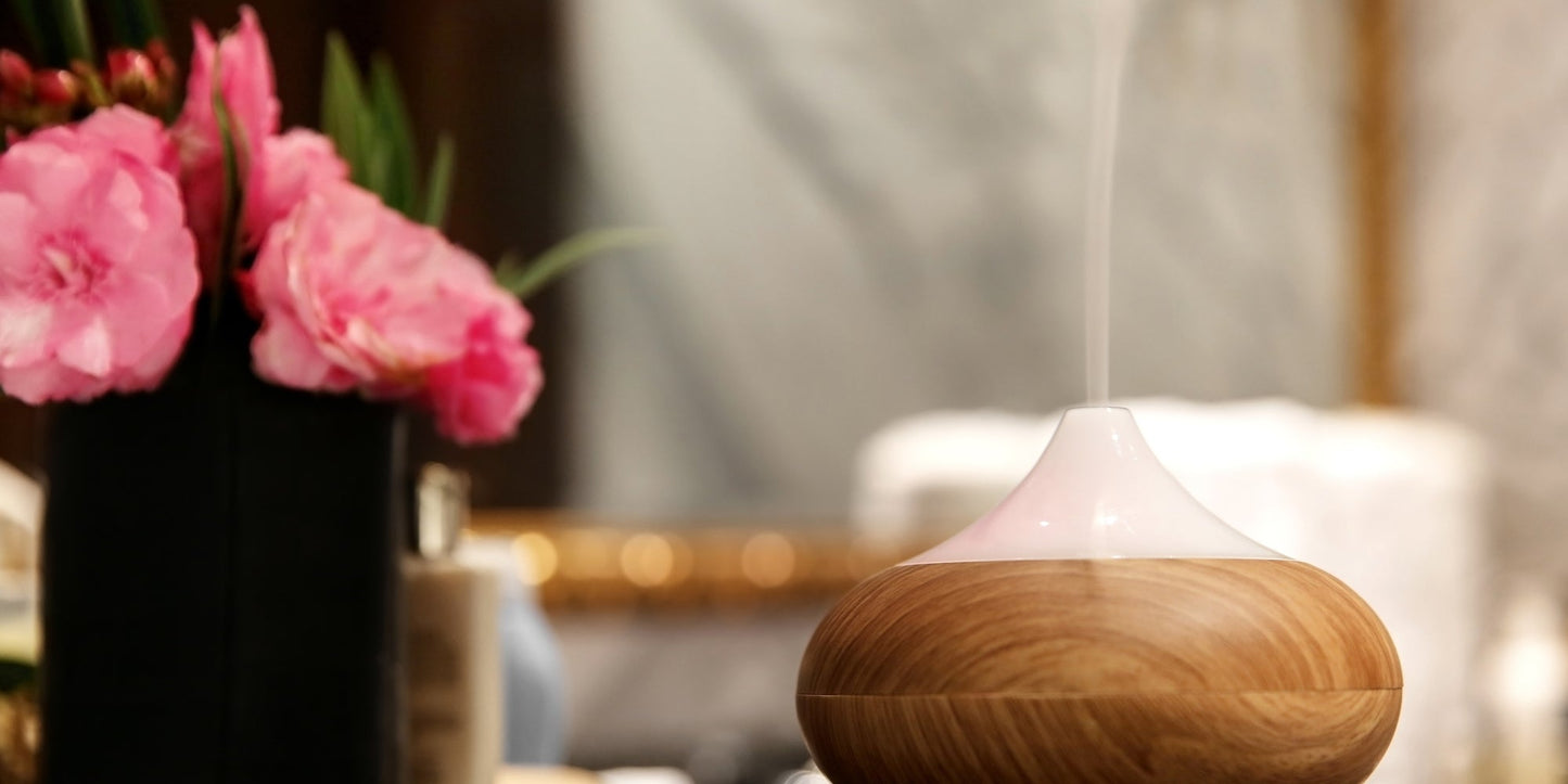 Ceramic ultrasonic diffuser releasing a fine mist of water and essential oils, surrounded by geranium flower buds and rose petals for a calming home aromatherapy ritual.